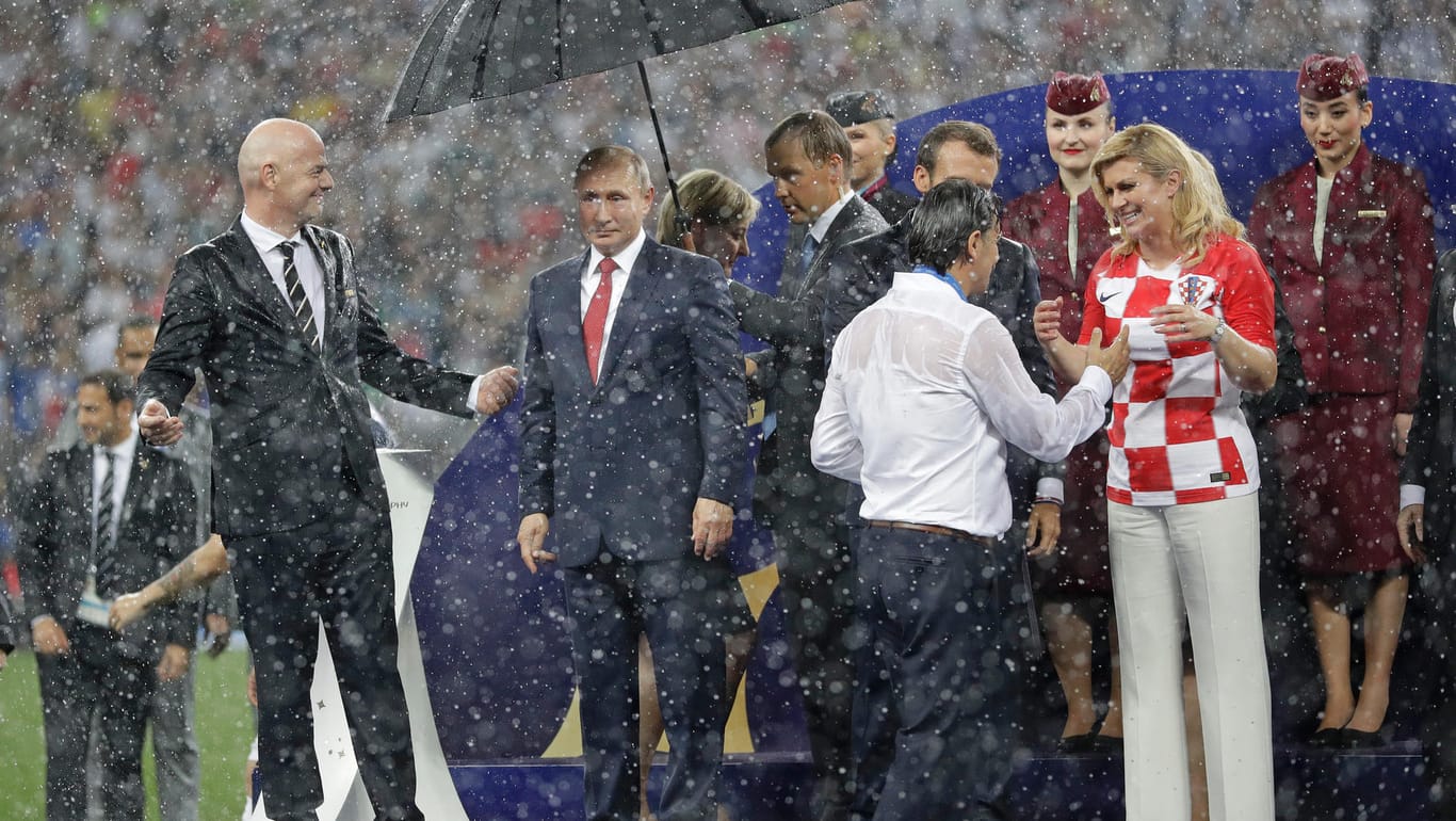 Starker Regen im Luschniki-Stadion: Während Wladimir Putin (2. v.l.) ein Schirm gereicht wird, werden die kroatische Präsidentin Kolinda Grabar-Kitarovic (vo. re. mit Trainer Zlatko Dalic) und Emmanuel Macron (l. daneben) pitschnass.
