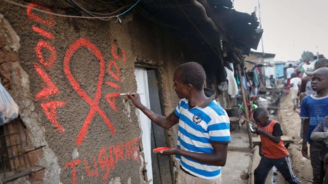 Ein junger Mann malt eine rote Aids-Schleife auf eine Wand im Kibera-Slum und schreibt in roten Buchstaben den Slogan "Avoid AIDS".