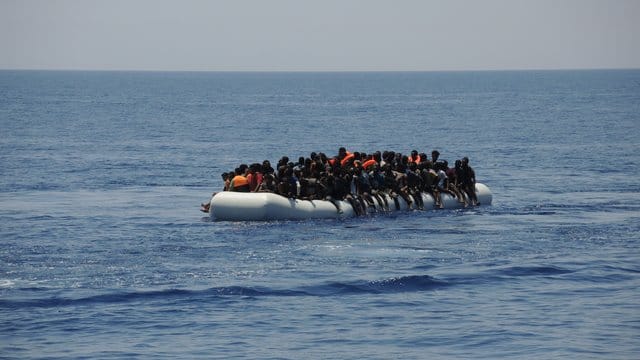 Migranten sitzen auf einem überladenen Schlauchboot im Mittelmeer.