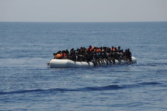Migranten sitzen auf einem überladenen Schlauchboot im Mittelmeer.