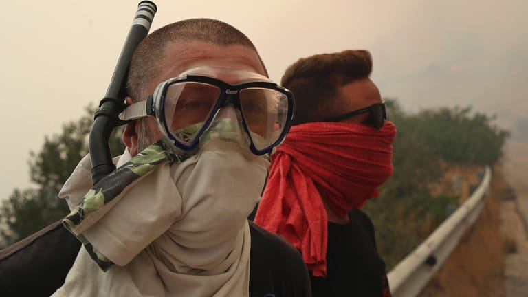Gefährlicher Rauch in Griechenland: Zwei Männer schützen sich mit Tüchern und einem Schnorchel vor dem Rauch eines Großbrandes.