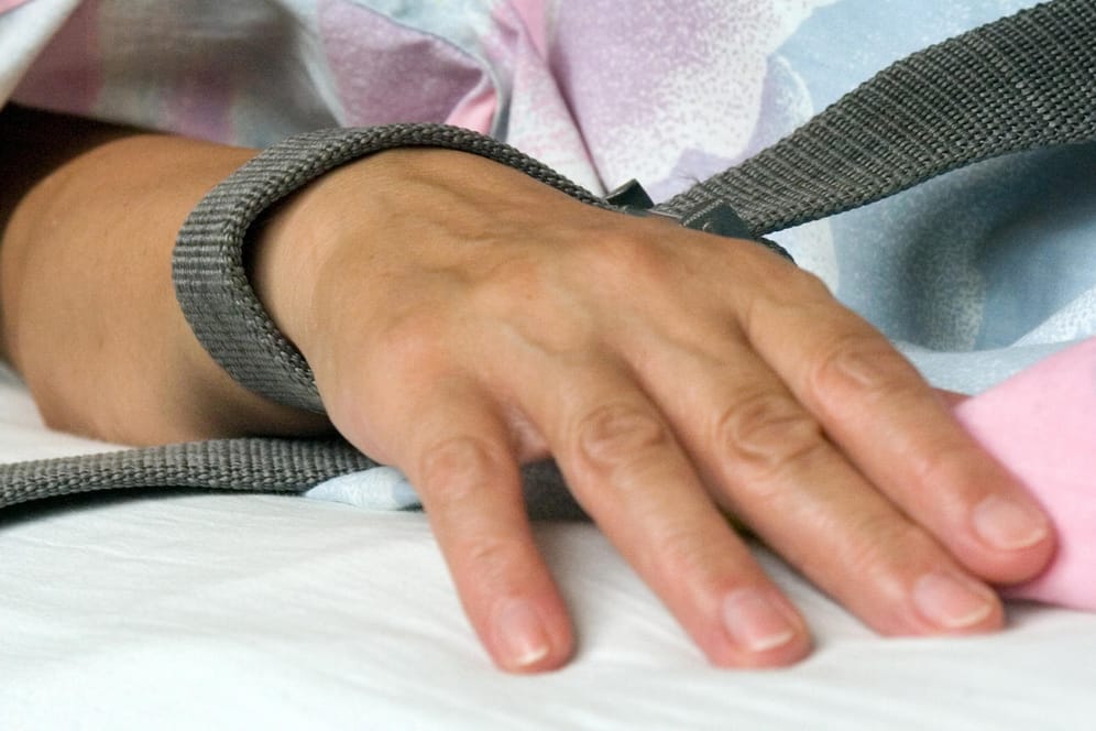 Eine mit einem Textilband festgebundene Hand eines Patienten: Die Fixierung beziehungsweise Fixation eines Patienten in der Krankenpflege durch Festschnallen am Handgelenk ist umstritten.