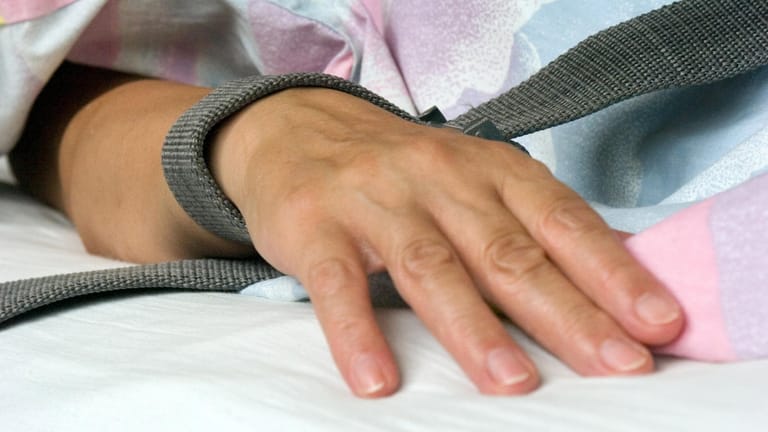 Eine mit einem Textilband festgebundene Hand eines Patienten: Die Fixierung beziehungsweise Fixation eines Patienten in der Krankenpflege durch Festschnallen am Handgelenk ist umstritten.