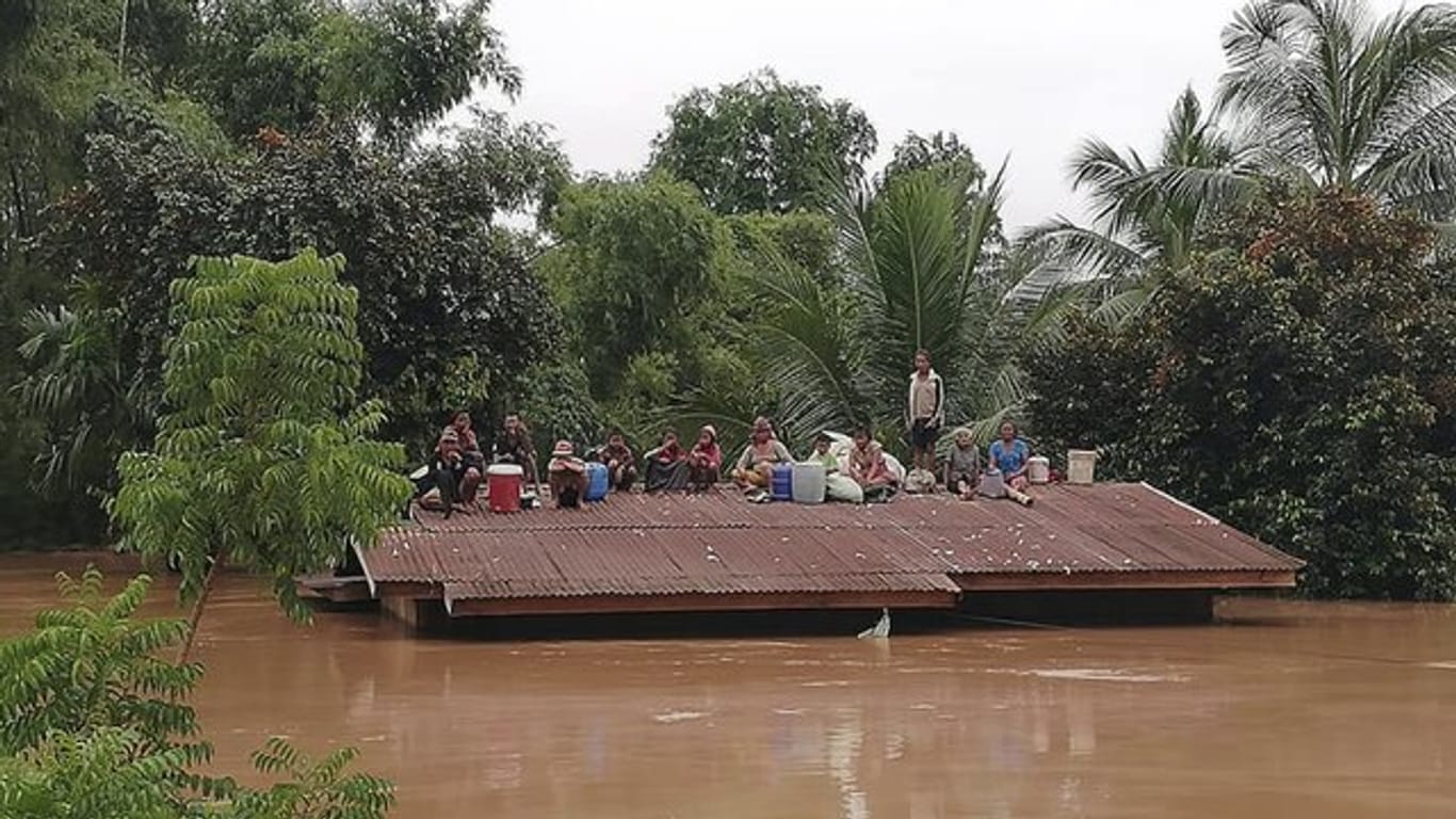 Dorfbewohner haben sich vor den Wassermassen aus dem eingestürzten Staudamm auf die Dächer eines Hauses gerettet.