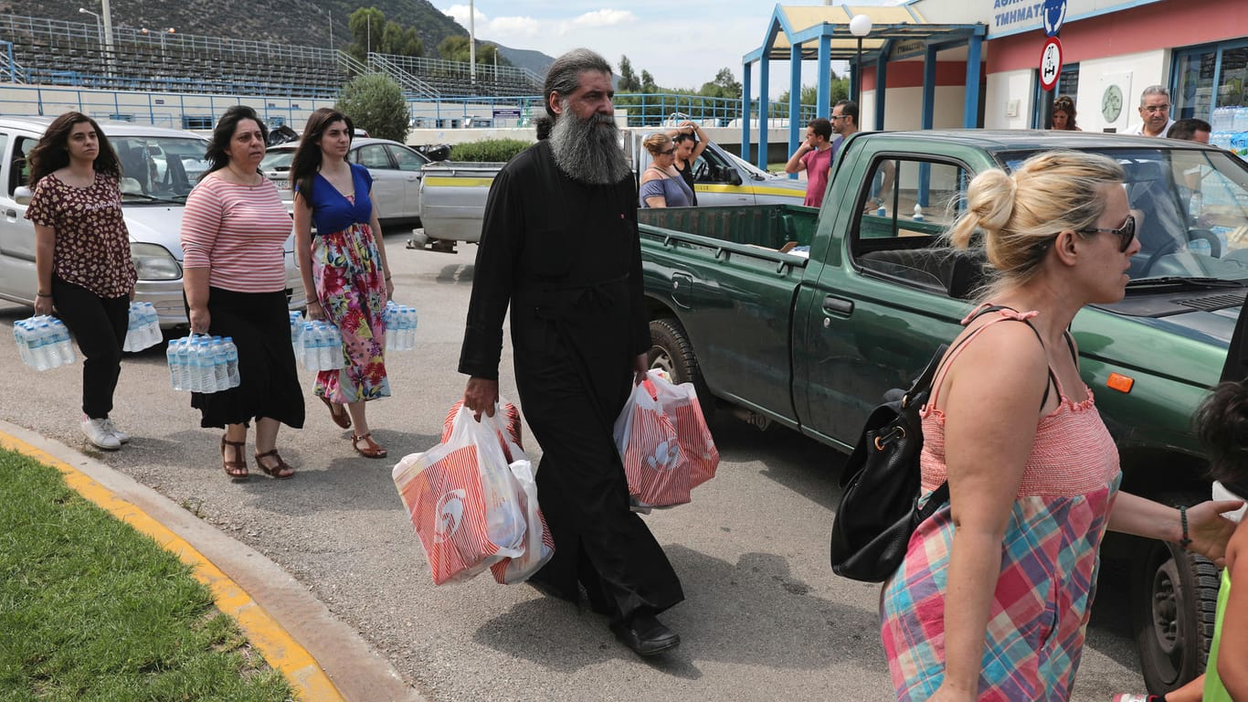 Menschen tragen Wasserflaschen und andere Vorräte aus einem kleinen Laden in Griechenland: Das griechische Wirtschaftsministerium sagte den betroffenen Regionen des Waldbrandes 20 Millionen Euro Soforthilfe zu.