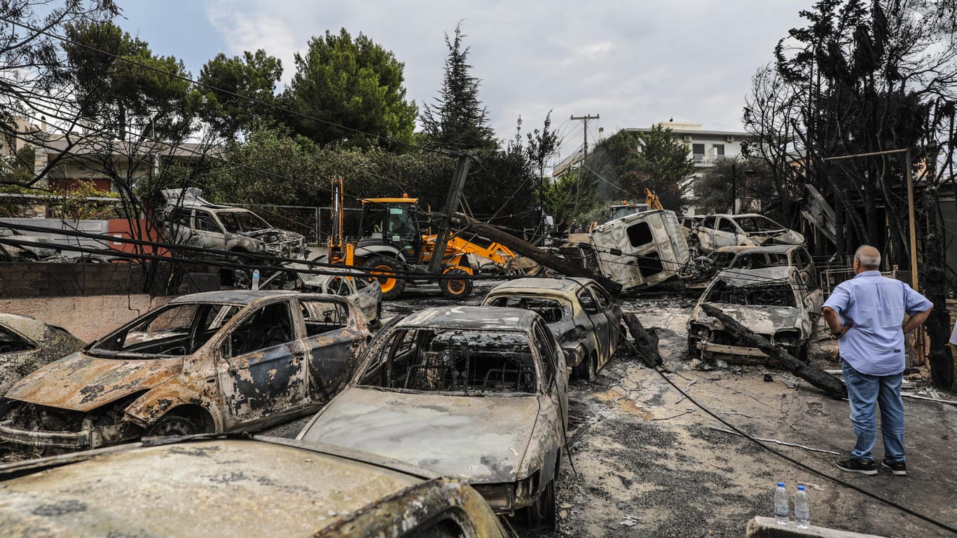 Ein Mann blickt auf verbrannte Fahrzeuge in der Küstenstadt östlich von Athen: Noch immer ist unklar, wie die Flammen so einen großen Schaden anrichten konnten.