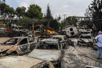 Ein Mann blickt auf verbrannte Fahrzeuge in der Küstenstadt östlich von Athen: Noch immer ist unklar, wie die Flammen so einen großen Schaden anrichten konnten.