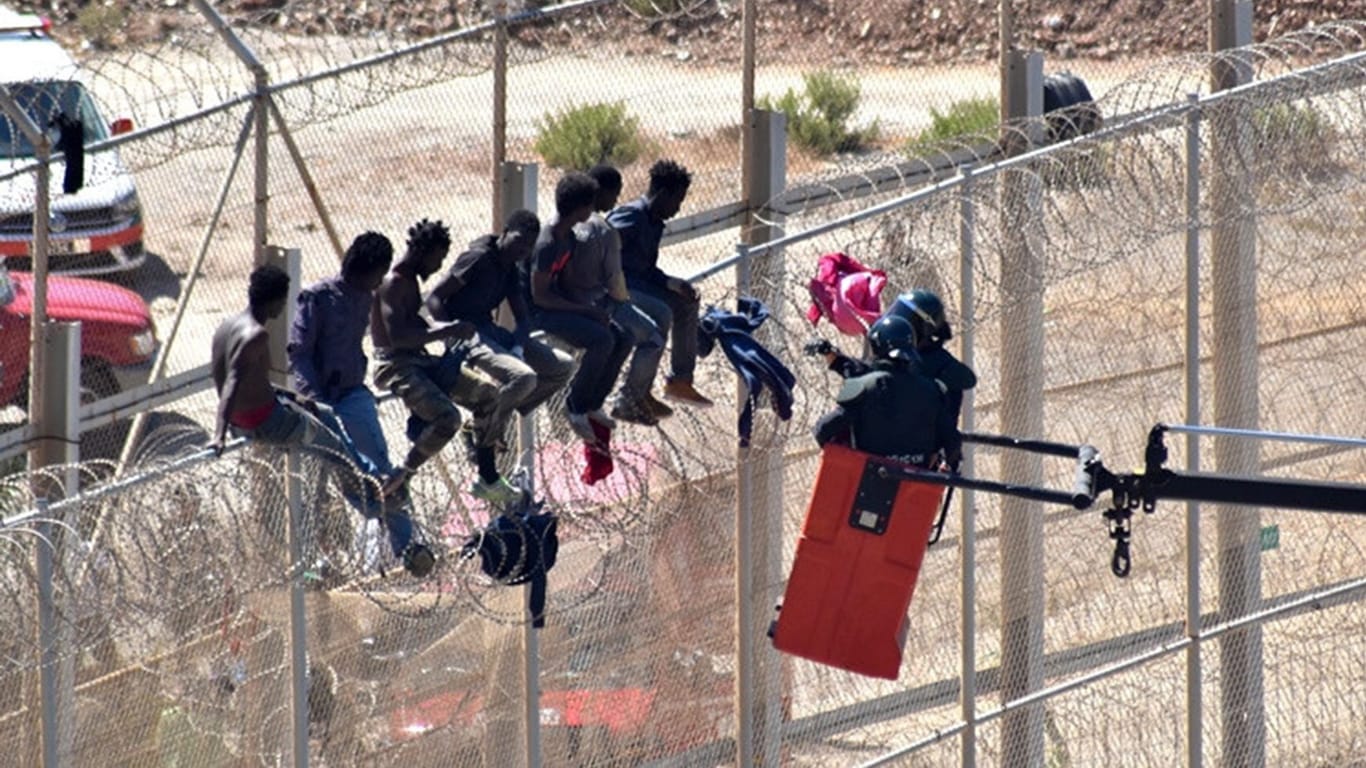 Migranten sitzen auf dem Grenzzaun in Ceuta, der die spanische Enklave von Marokko trennt: Spanien will die messerscharfen Klingen von den Zäunen entfernen.