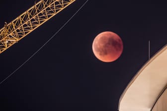 Frankfurt am Main: Zwischen einem Baukran und einem Gebäude in der Innenstadt ist der rötlich gefärbte Vollmond zu sehen: Bei der längsten Mondfinsternis des 21. Jahrhunderts taucht der Mond in den Erdschatten ein.