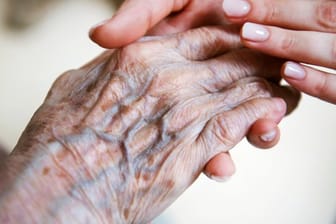 Eine Pflegerin hält die Hand einer alten Frau.