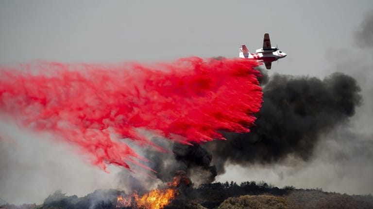 Ein Flugzeug lässt Löschmittel auf einen Waldbrand fallen.