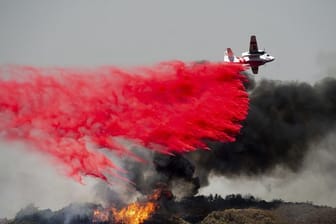 Ein Flugzeug lässt Löschmittel auf einen Waldbrand fallen.