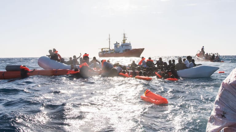 Start in Libyen: Flüchtlinge werden aus dem Mittelmeer geborgen. Meist übernimmt das inzwischen die libysche Küstenwache – und die bringt die Menschen zurück. Auf dem Foto ist im Hintergrund das Rettungsschiff "Aquarius", das nun wieder in die Such- und Rettungszone zurückkehrt.