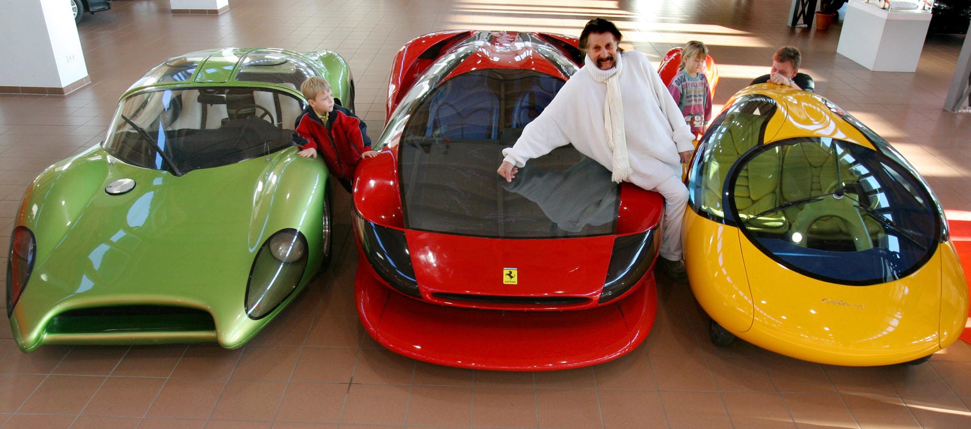 "Das gelbe Ei": Luigi Colani im Jahr 2006 mit seinem neuentwickelten Stadtauto (r.), einem Ferrari Testarossa (M.), mit dem er einen Weltrekord von 387 km/h gefahren hat, und einem Speedster auf Basis eines VW-Käfers von 1968/69 (l.) in einem Autohaus.
