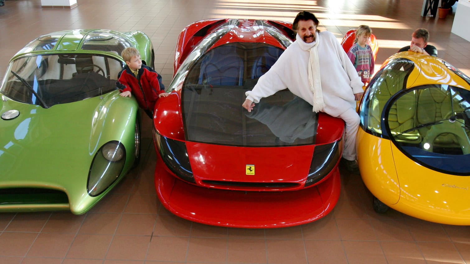 "Das gelbe Ei": Luigi Colani im Jahr 2006 mit seinem neuentwickelten Stadtauto (r.), einem Ferrari Testarossa (M.), mit dem er einen Weltrekord von 387 km/h gefahren hat, und einem Speedster auf Basis eines VW-Käfers von 1968/69 (l.) in einem Autohaus.