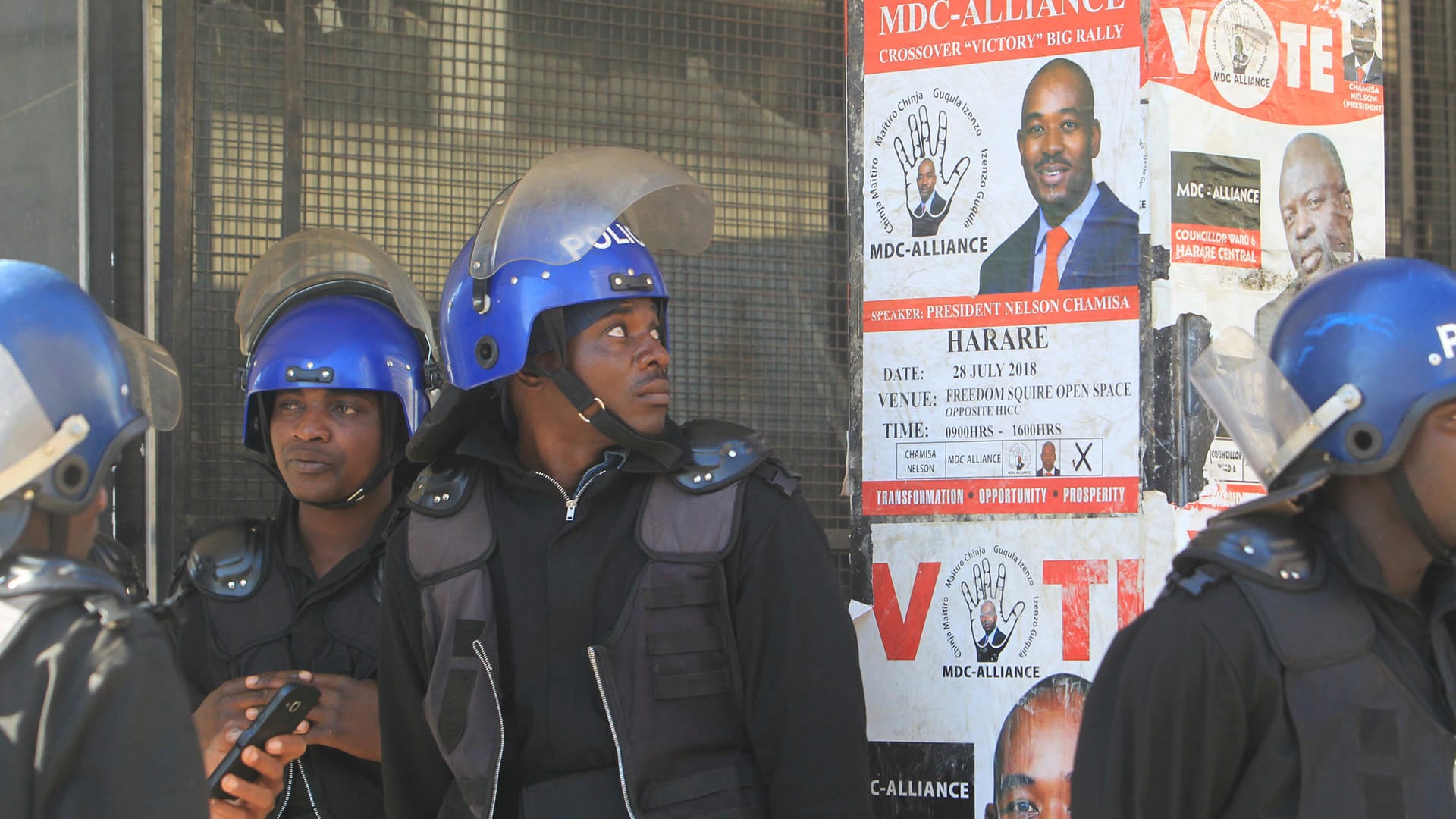 Polizisten vor einem Wahlplakat des wichtigsten Oppositionsführers in Simbabwe: Nach Protesten hat die Polizei die Zentrale der Opposition gestürmt.