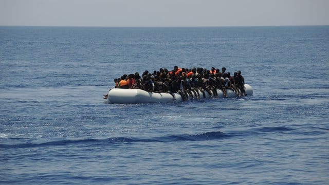 Migranten sitzen auf einem überladenen Schlauchboot im Mittelmeer. Migranten sitzen auf einem überladenen Schlauchboot im Mittelmeer.