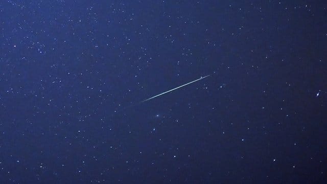 Eine Sternschnuppe leuchtet am Nachthimmel.