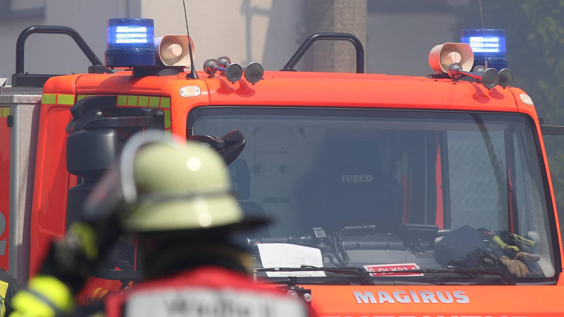 Feuerwehrmann vor einem Feuerwehrwagen mit Blaulicht: In der Nähe von Köln kam es zu einem Feuer in einer Flüchtlingsunterkunft.