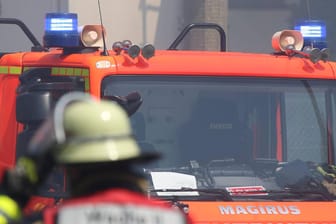 Feuerwehrmann vor einem Feuerwehrwagen mit Blaulicht: In der Nähe von Köln kam es zu einem Feuer in einer Flüchtlingsunterkunft.