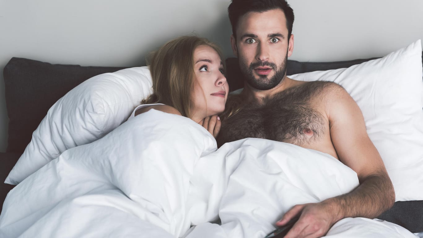 Paar schaut Fernsehen im Bett: Ablenkung im Schlafzimmer schlägt sich auch auf das Liebesleben nieder.