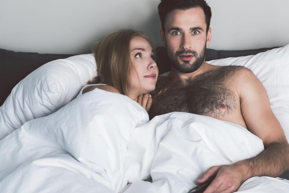 Paar schaut Fernsehen im Bett: Ablenkung im Schlafzimmer schlägt sich auch auf das Liebesleben nieder.