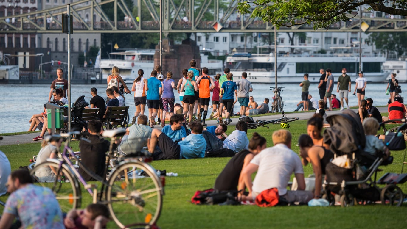 Viele Menschen sitzen bei sommerlichen Temperaturen am Mainufer bei Frankfurt: Am Wochenende soll es entspannte Sommertemperaturen geben.