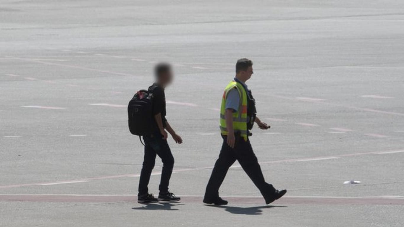 Der Mann wird in Begleitung eines Bundespolizisten am Flughafen Tegel zu einem Einsatzfahrzeug geführt.