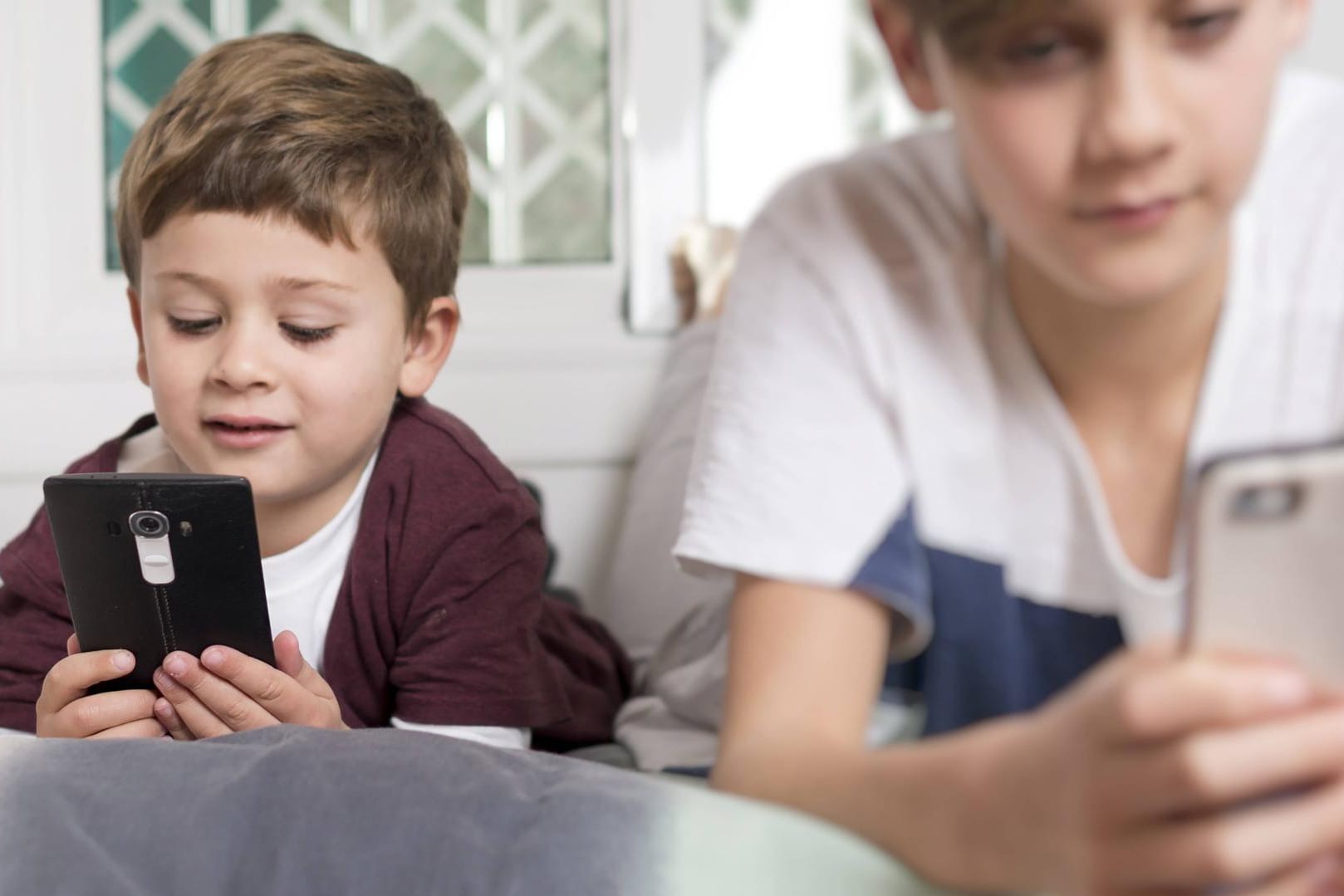 Zwei Kinder mit Smartphones: Wer in jungen Jahren zu viel aufs Handy schaut, hat ein höheres Risiko kurzsichtig zu werden.