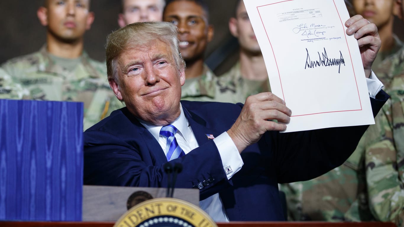 US-Präsident Donald Trump zeigt in der Militärbasis Fort Drum ein frisch unterzeichnetes Gesetz: Das Gesetz sieht für 2019 erhöhte Ausgaben in einem Umfang von 716 Milliarden Dollar für Rüstung und Militär vor.