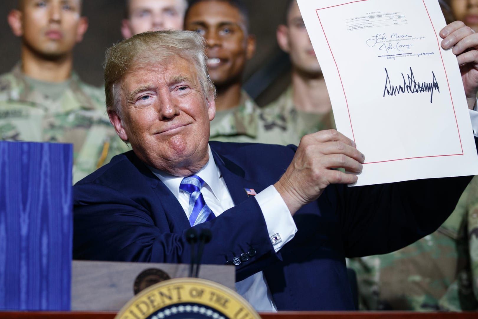 US-Präsident Donald Trump zeigt in der Militärbasis Fort Drum ein frisch unterzeichnetes Gesetz: Das Gesetz sieht für 2019 erhöhte Ausgaben in einem Umfang von 716 Milliarden Dollar für Rüstung und Militär vor.