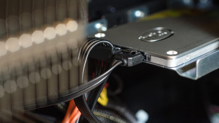 Eine 2,5-Zoll-SSD im Laufwerksschacht eines Desktop-PCs: In SSDs stecken keine rotierenden Magnetscheiben, sondern Flash-Bausteine. (Archivbild)
