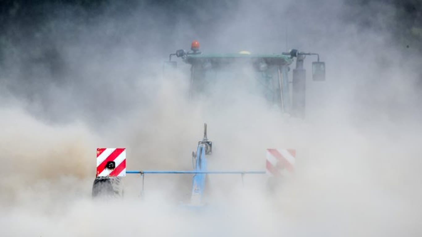 Ein Traktor zieht auf einem trockenen Feld in Kühdorf (Thüringen) eine große Staubwolke hinter sich her.