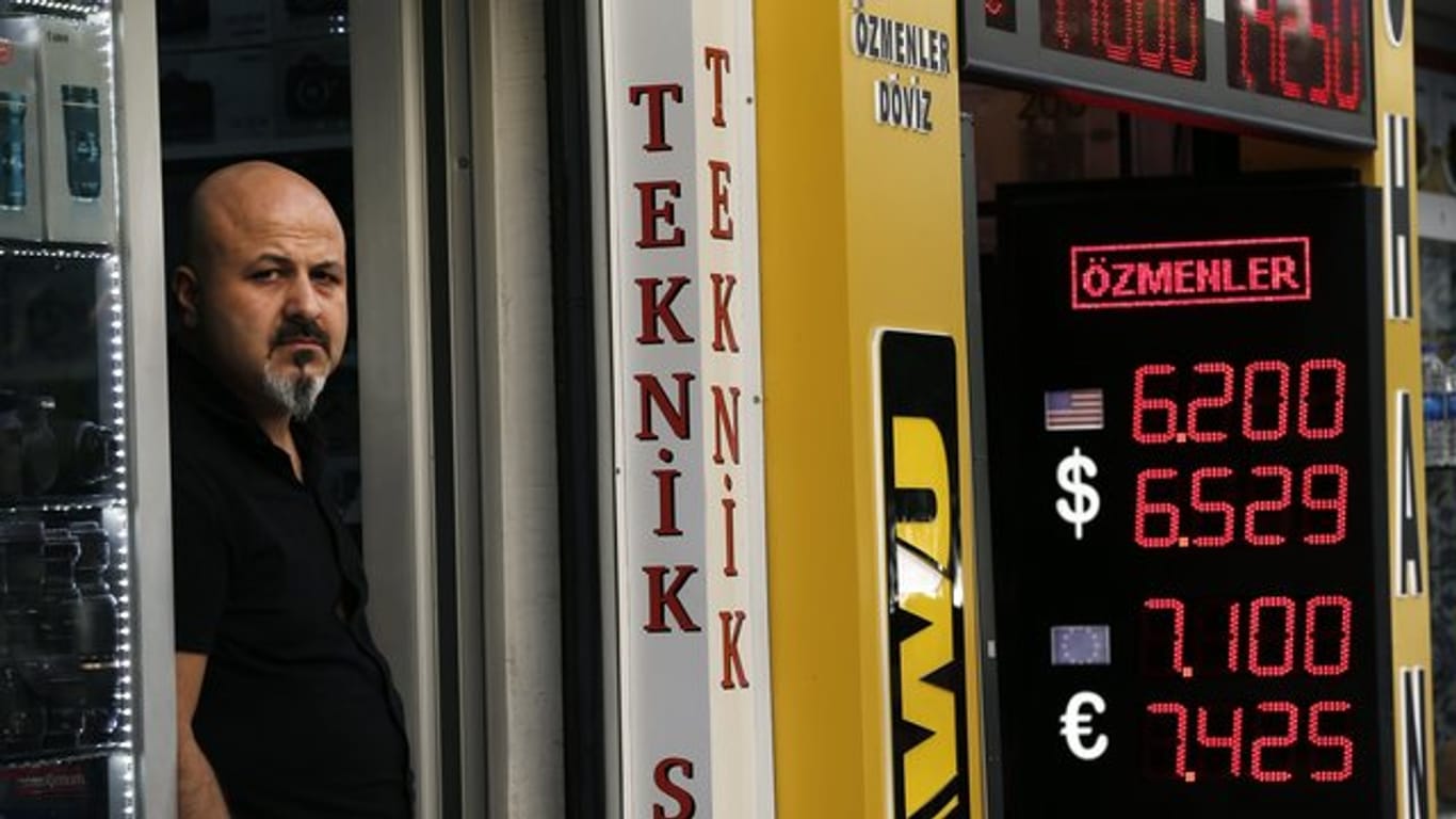 Ein Ladenbesitzer steht neben einer Anzeigetafel, die die Wechselkurse der türkischen Lira anzeigt.