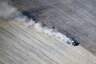 Eine dichte Staubwolke zieht ein Traktor bei Feldarbeiten hinter sich her: Einem Medienbericht zufolge melden Bundesländer Dürreschäden in Milliardenhöhe an.