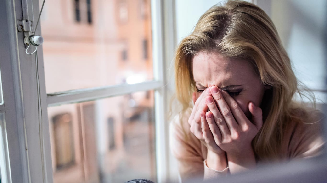 Woman sitting on windowsill, looking out of window, crying