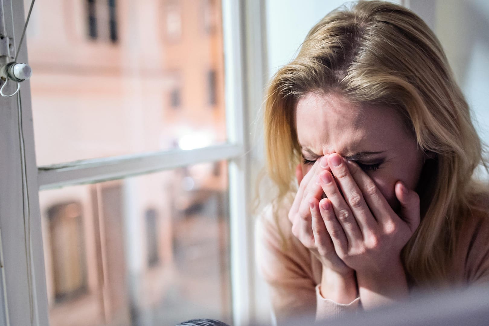 Woman sitting on windowsill, looking out of window, crying