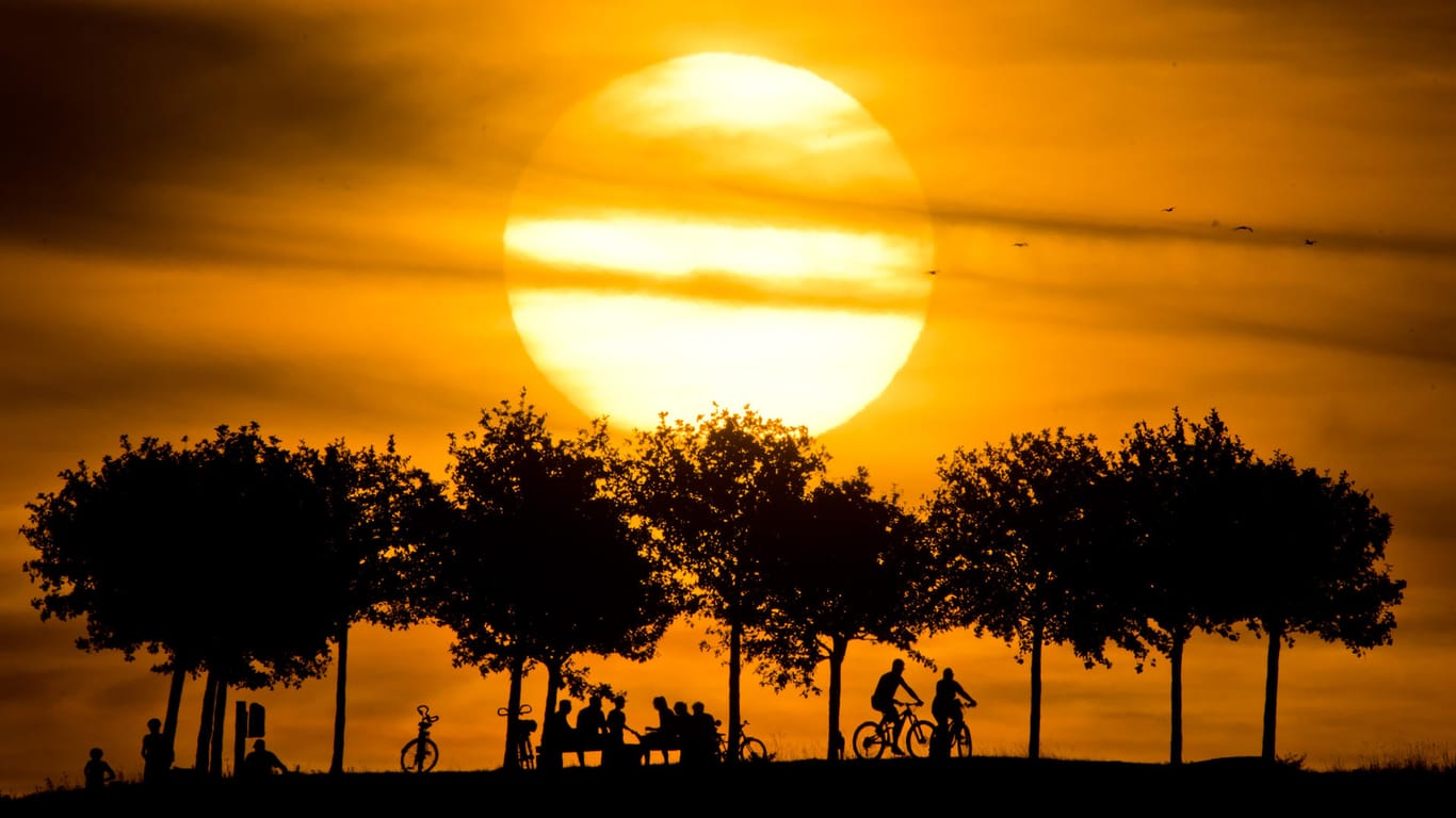 Die Silhouetten von Passanten zeichnen sich vor einem Sonnenuntergang ab: Der Sommer 2018 ist trotz Hitze und Dürre nicht auf Rekordkurs.