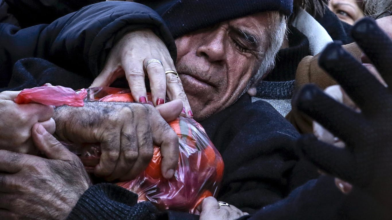 Januar 2016: Bei einer Essensausgabe in Athen hält ein Mann einen Beutel Mandarinen in den Armen während andere an ihm zerren.