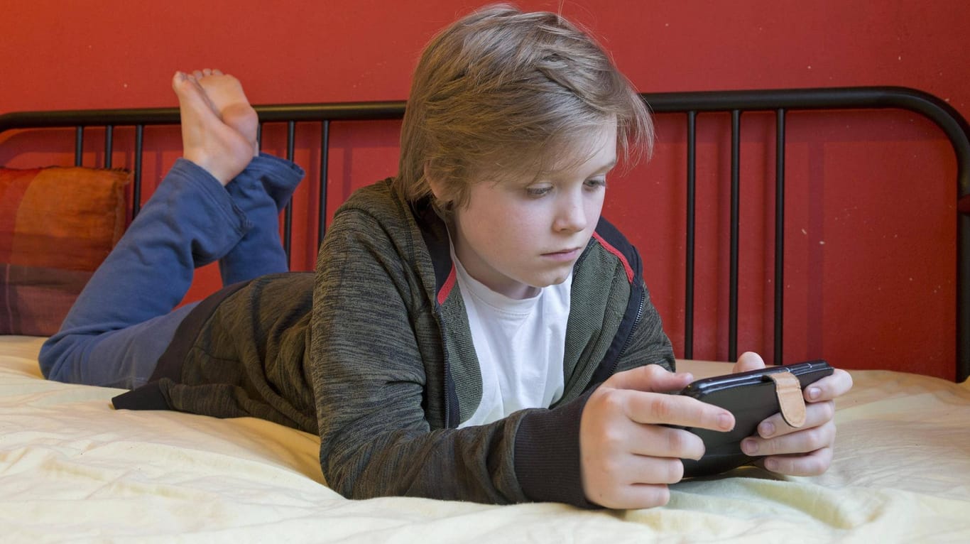 Junge mit Smartphone liegt auf seinem Bett: Machen Smartphone-Spiele süchtig? Ein Experte meint: Ja!