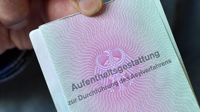 Ein Mann aus Syrien zeigt in einer Gemeinschaftsunterkunft für Flüchtlinge seine "Aufenthaltsgestattung". Ein Mann aus Syrien zeigt in einer Gemeinschaftsunterkunft für Flüchtlinge seine "Aufenthaltsgestattung".