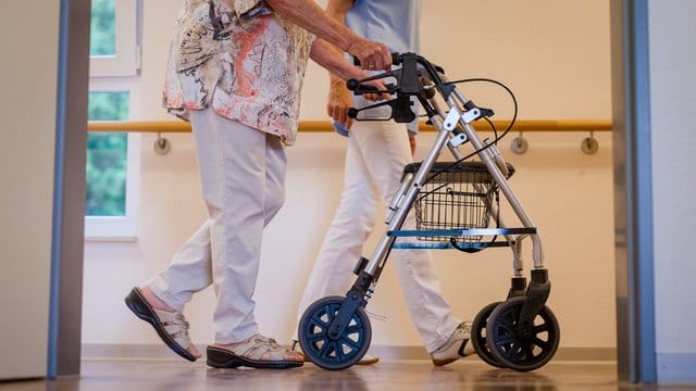 Eine Pflegekraft begleitet in einem Pflegeheim eine ältere Dame über einen Korridor. Eine Pflegekraft begleitet in einem Pflegeheim eine ältere Dame über einen Korridor.