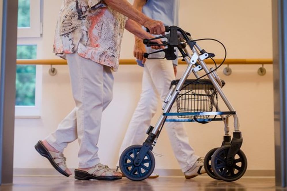 Eine Pflegekraft begleitet in einem Pflegeheim eine ältere Dame über einen Korridor.