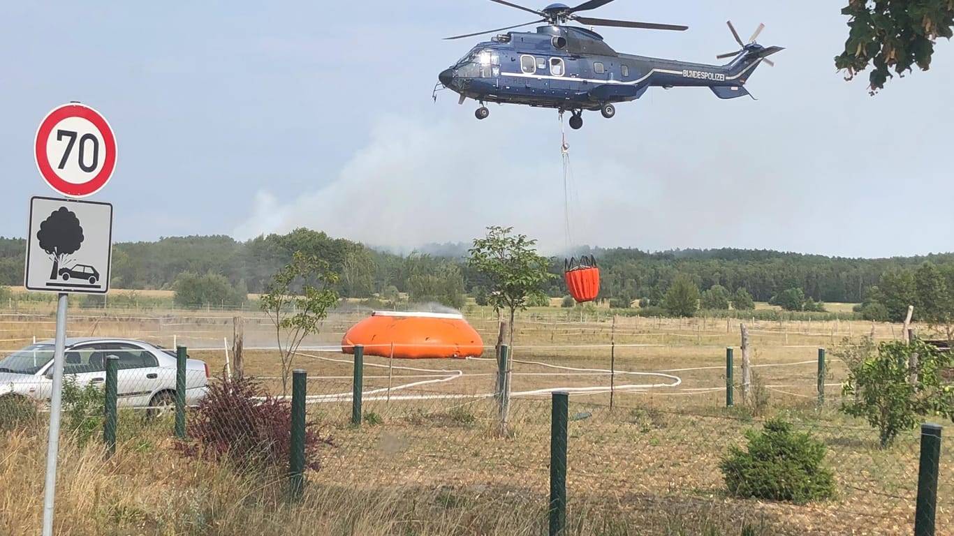 Rauch im Hintergrund: Ein Polizeihubschrauber holt Wasser und wirft es aus der Luft an, keine fünf Minuten später ist er wieder da.