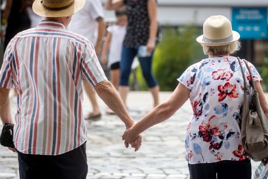 Zwei ältere Menschen mit überqueren Hand in Hand einen Fußgängerüberweg.