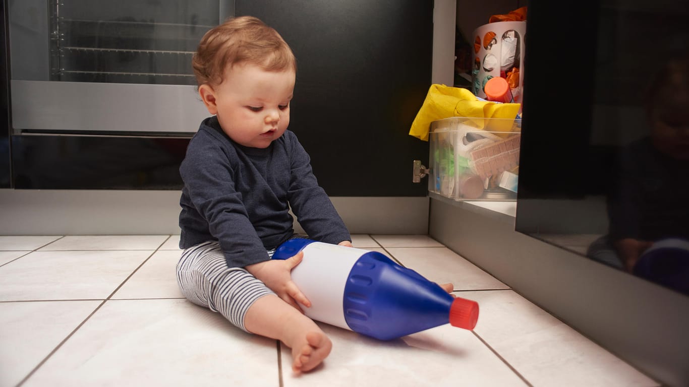 Kind zieht Putzmittel aus einem Schrank: Auch im Haushalt besteht die Gefahr, sich zu vergiften.