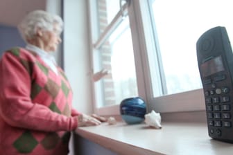 Eine alte Frau steht neben einem Telefonhörer: Falsche Polizisten am Telefon haben Senioren schon um ihre gesamten Ersparnisse gebracht. (Symbolbild)