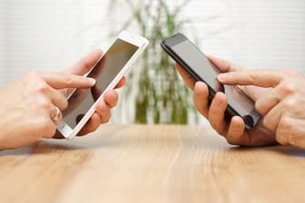 Zwei Smartphone-Nutzer sitzen sich gegenüber: Mit der Cringle-App konnten Nutzer Geld an ihre Freunde überweisen.