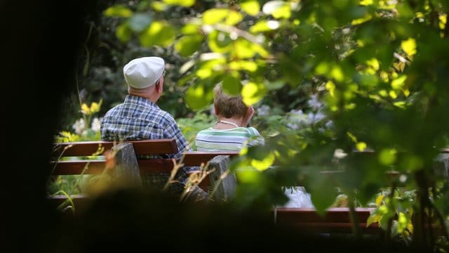 Ein älteres Paar sitzt im Kurpark auf einer Bank im Sonnenschein. Ein älteres Paar sitzt im Kurpark auf einer Bank im Sonnenschein.