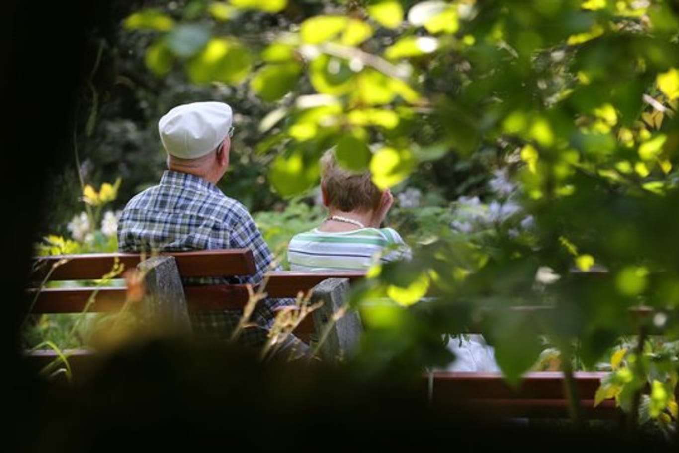 Ein älteres Paar sitzt im Kurpark auf einer Bank im Sonnenschein.